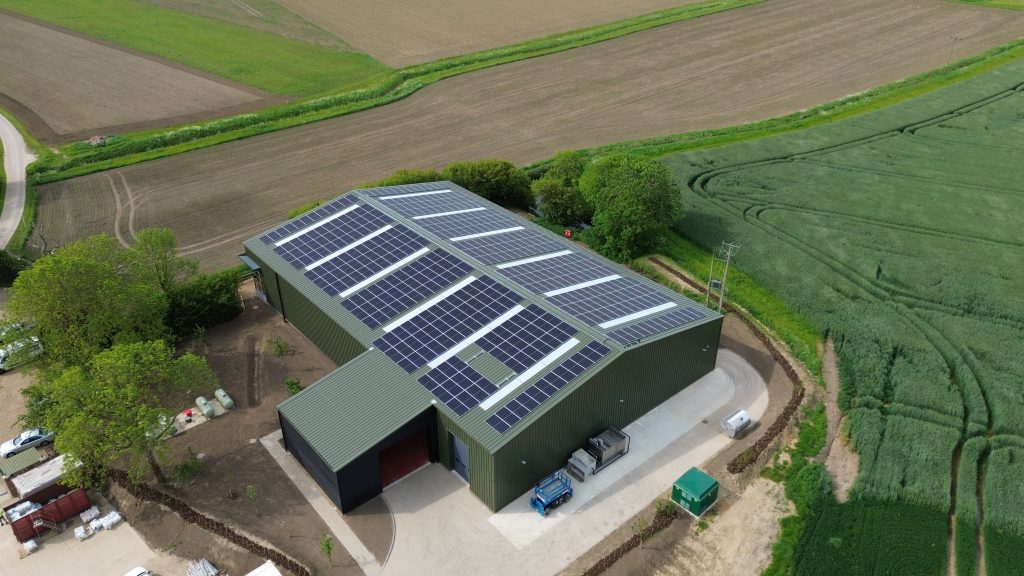 Roof mounted solar installation on metal barn roof surrounded by farmland